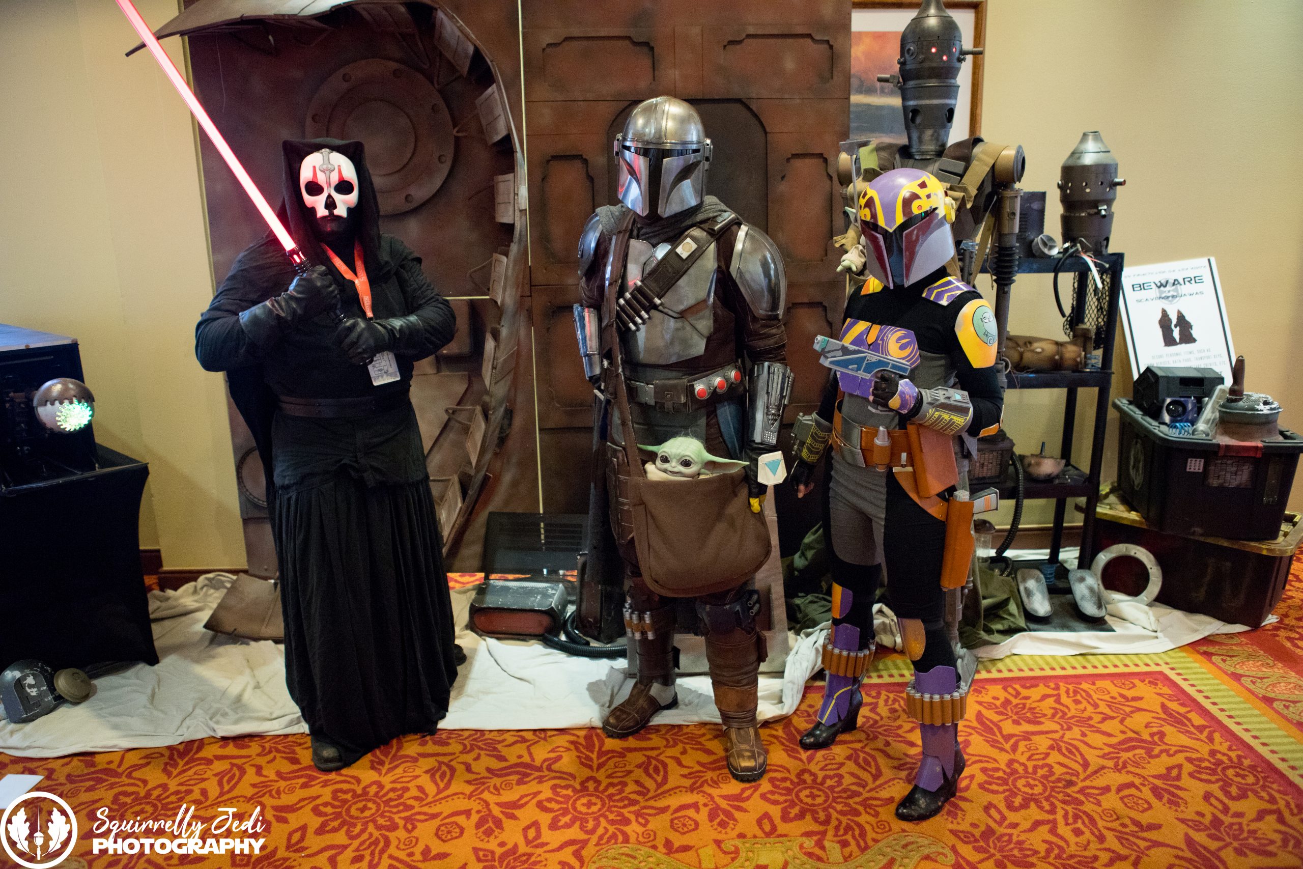 Three cosplayers pose for a photo in Star Wars costumes. Two are Mandalorian. 